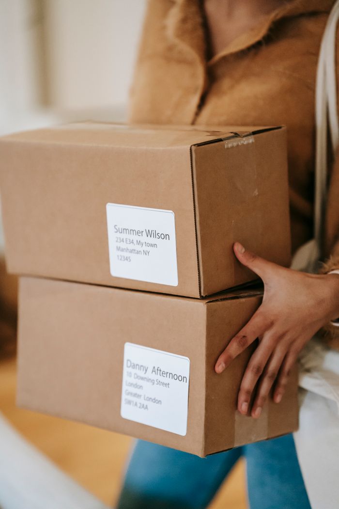 About Crop anonymous female in casual clothes bringing carton parcels with address labels in post office