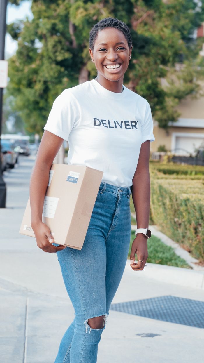 About Happy delivery woman holding a package in an outdoor setting, representing modern courier services.