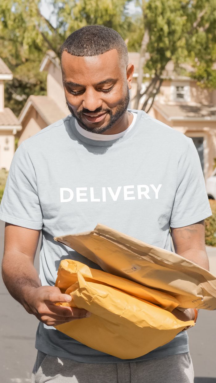 A cheerful delivery professional holding parcels outside a suburban home.
